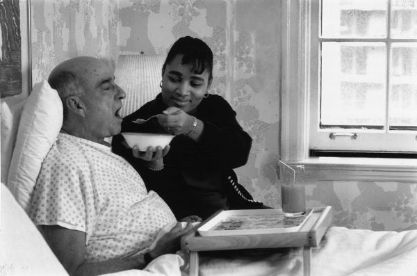 Hospice worker feeding an elderly patient in bed.